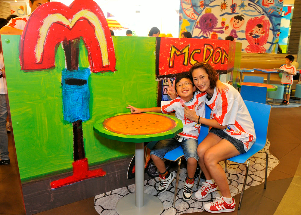 A child's crayon drawing of a McDonald's, built at full scale — a boy and an adult sit at the hand-painted table inside it